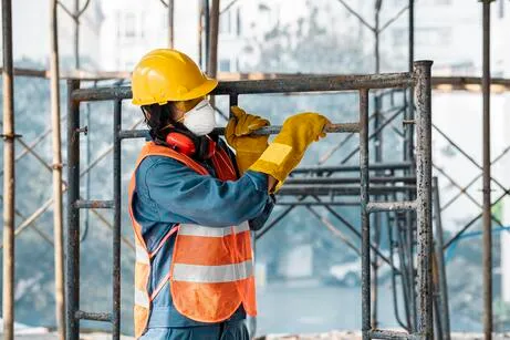 Homem na construção com equipamentos de segurança carregando um andaime desmontado